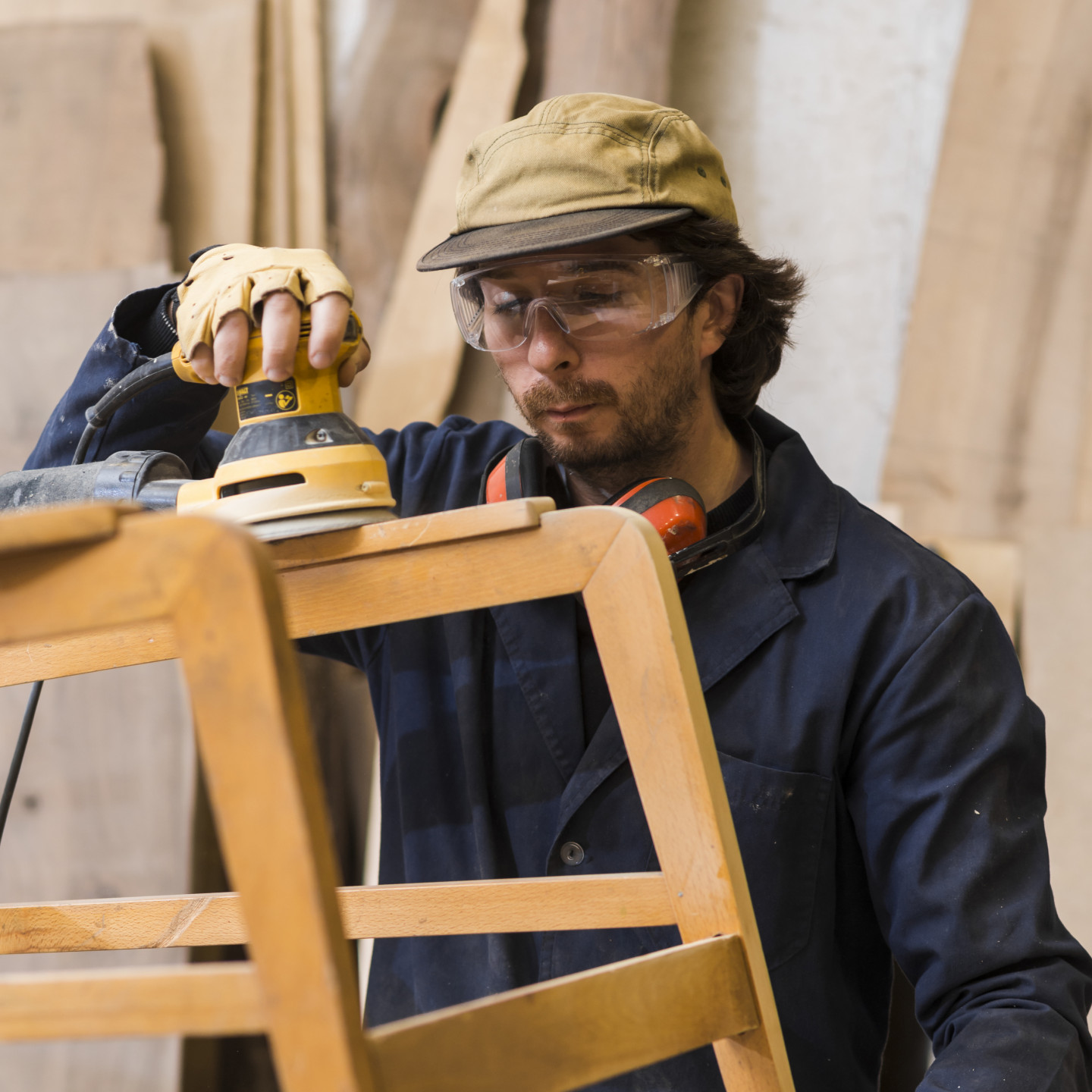 man-wearing-safety-eyeglasses-working-with-orbital-sanders-wooden-furniture